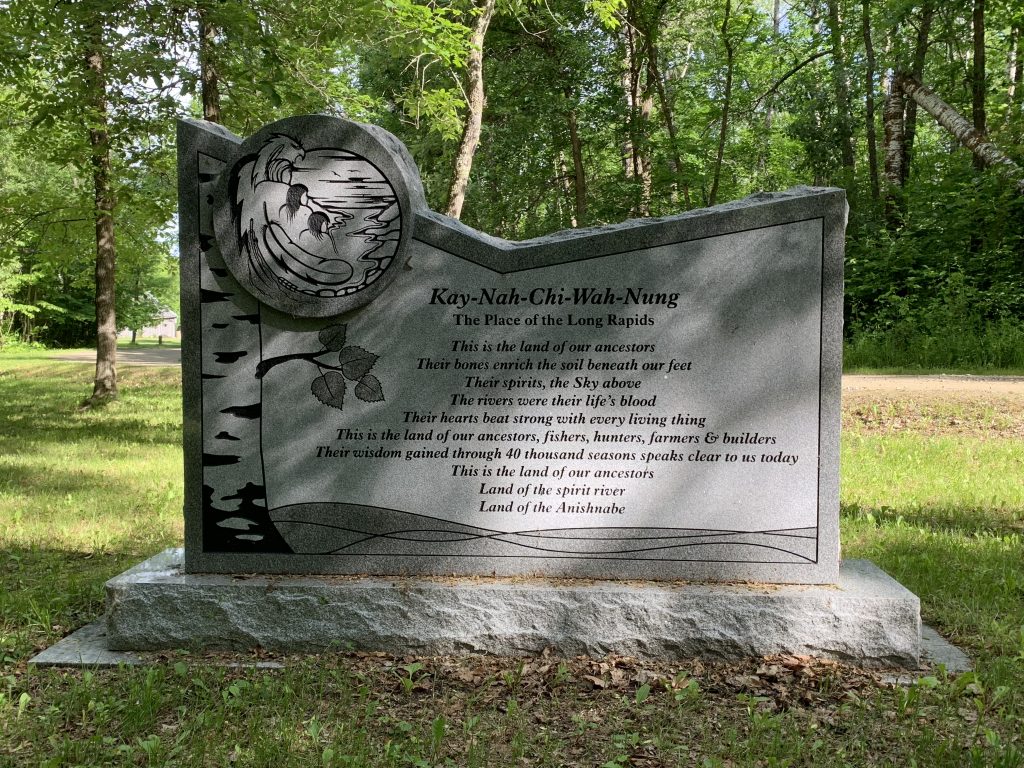 Stone monument with images and text, with trees in the background.